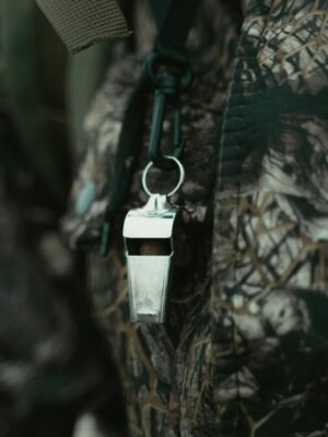 Close-up of a shiny silver whistle hanging against a camouflage-patterned fabric background.