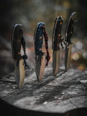 Four sharp knives with patterned handles displayed vertically on a wooden surface outdoors.