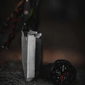 A survival knife with a tactical wristwatch set on rocks in a forest setting, showcasing outdoor adventure gear.