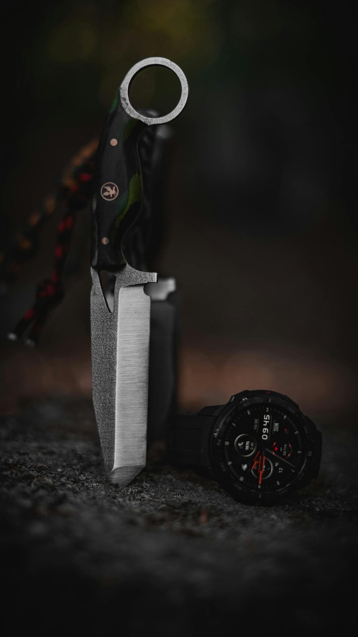 A survival knife with a tactical wristwatch set on rocks in a forest setting, showcasing outdoor adventure gear.