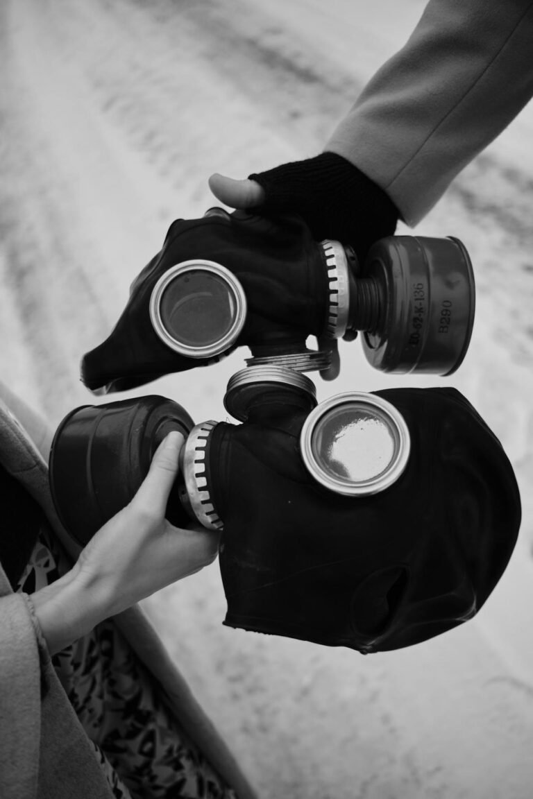 Black and white close-up of hands holding two gas masks, symbolizing caution.