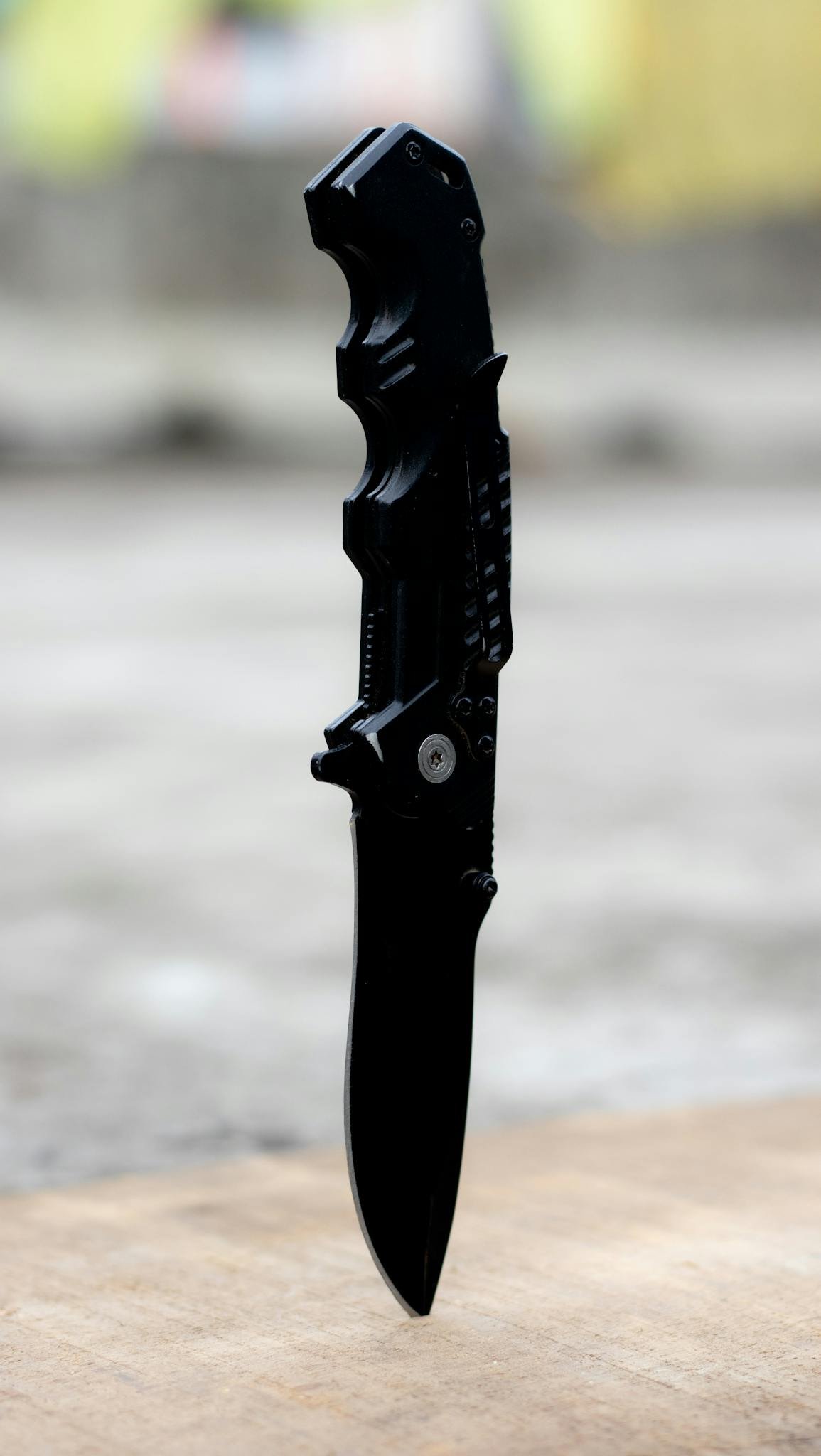 High-quality image of a black folding knife standing on a wooden surface outdoor.
